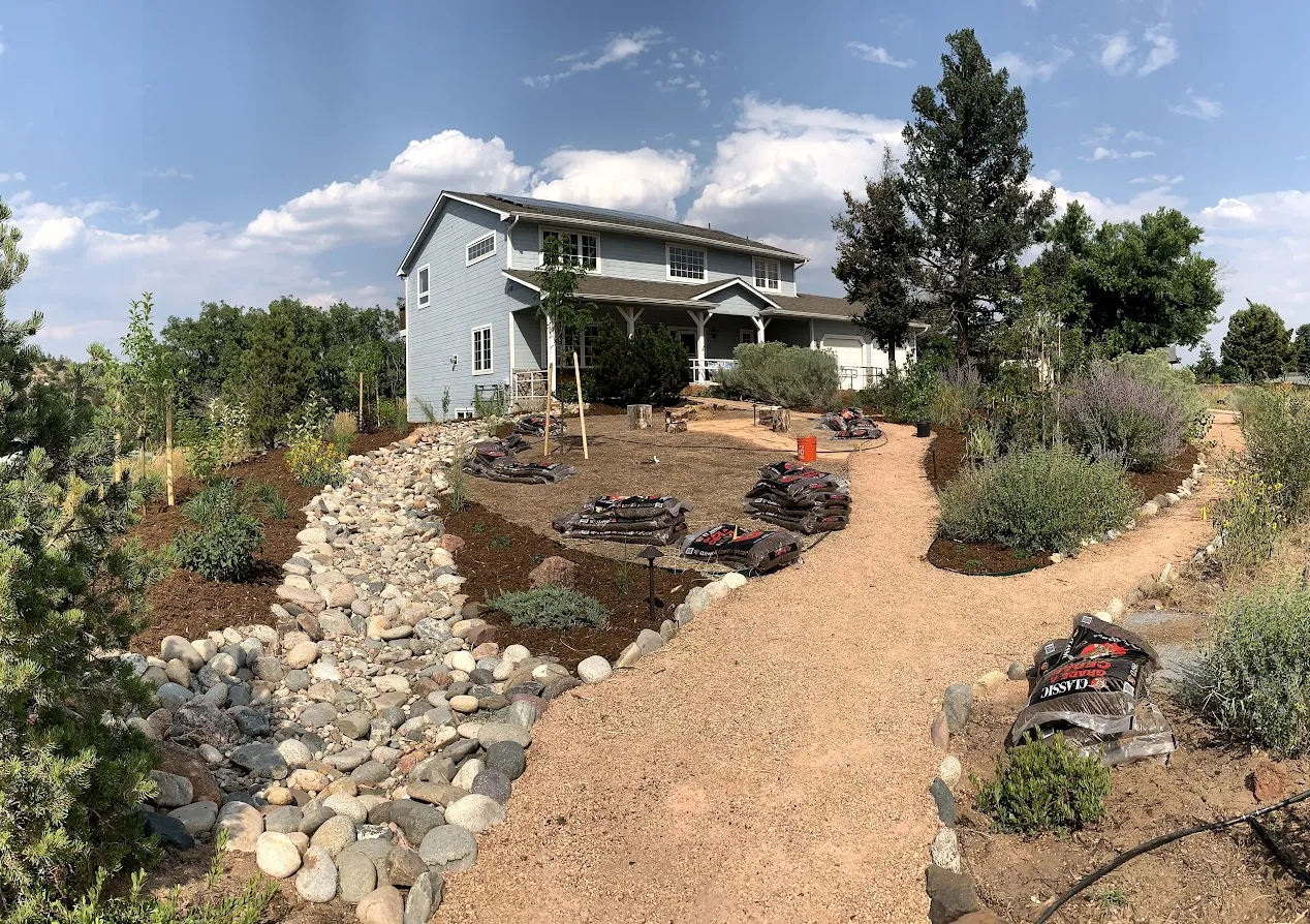 blue residential house with trees and plantings and blue sky with clouds